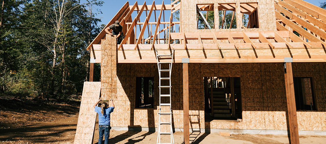 Two people work on building the frame for a new home