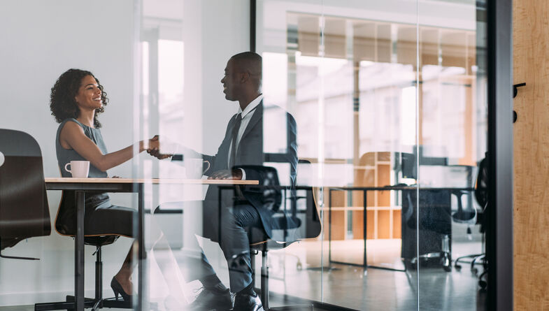 Two businesspeople shaking hands in a glass office
