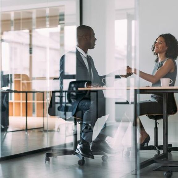 Two businesspeople shaking hands in a glass office