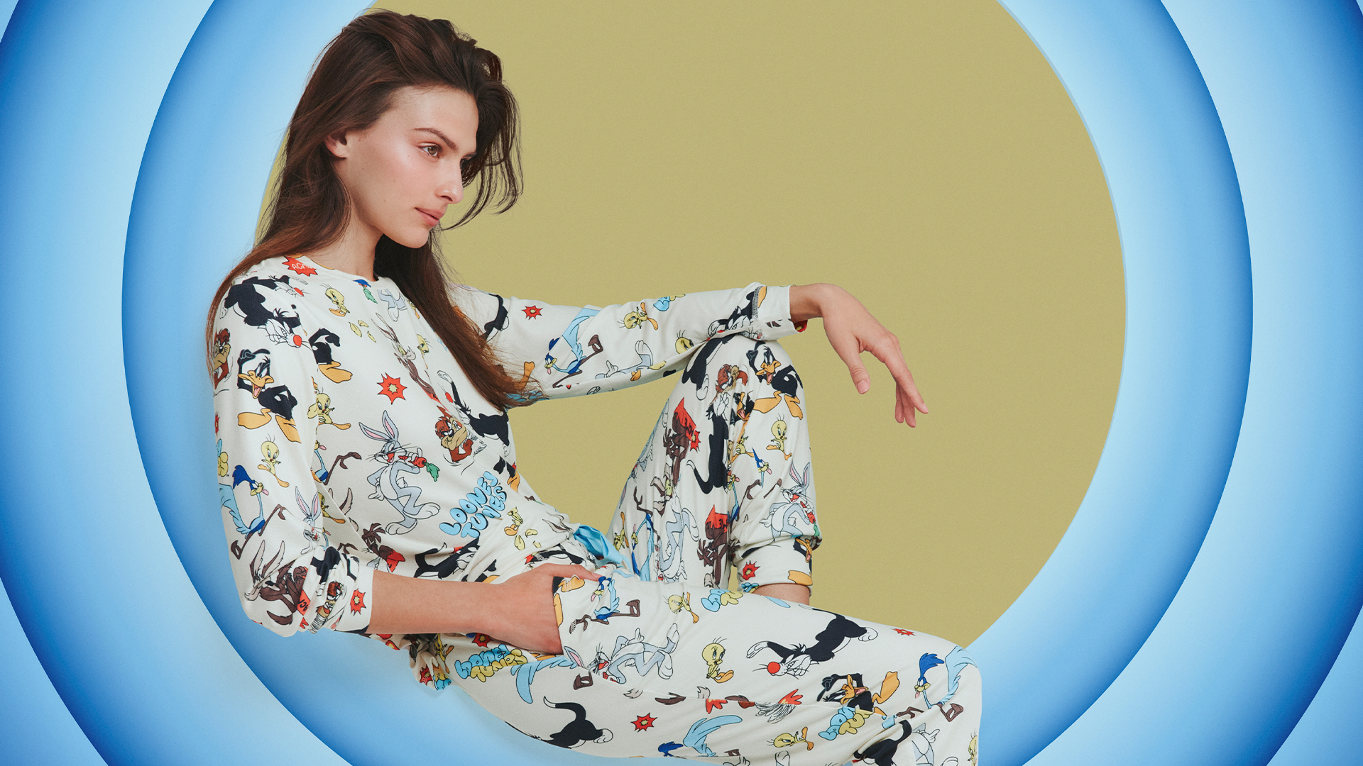 woman in cosy looney tunes themed pyjamas lies on the looney tunes background
