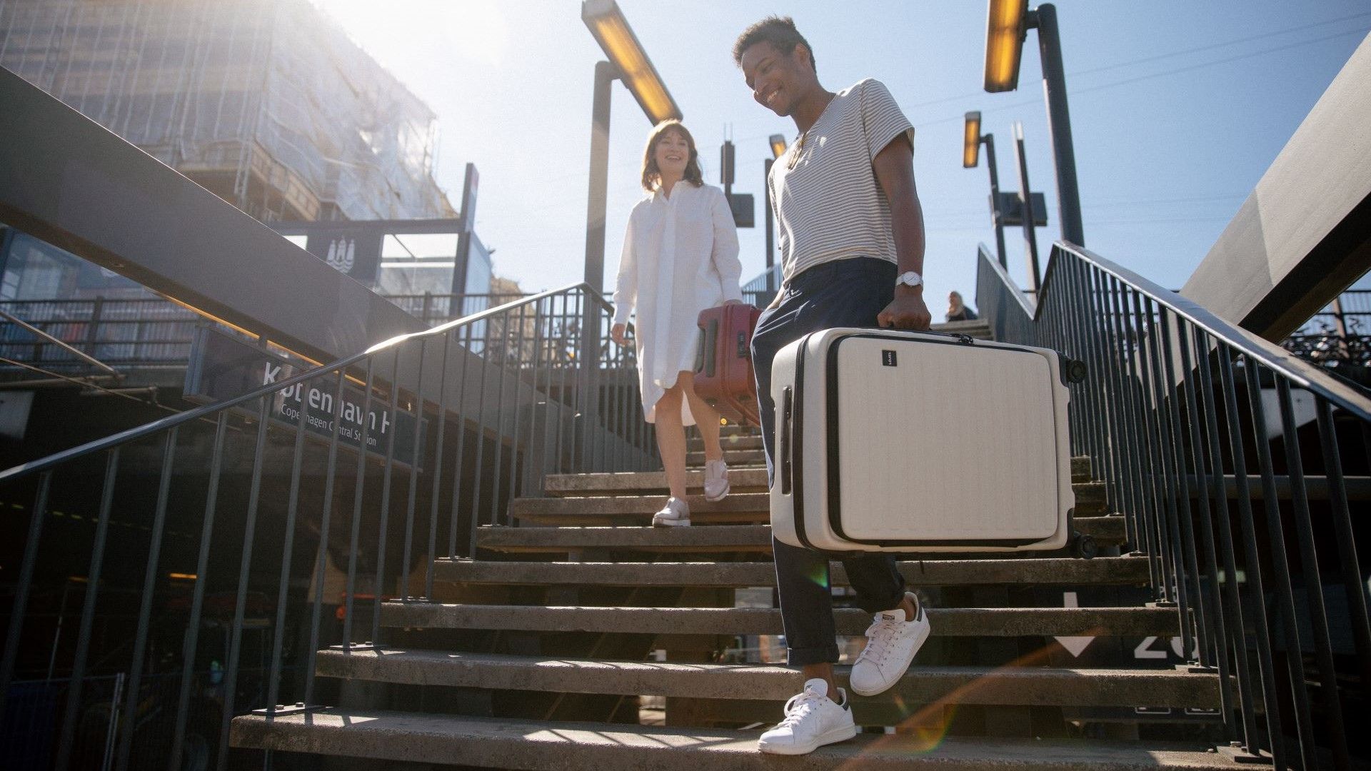 man and women walking down train station stairs holding luggage in their hand