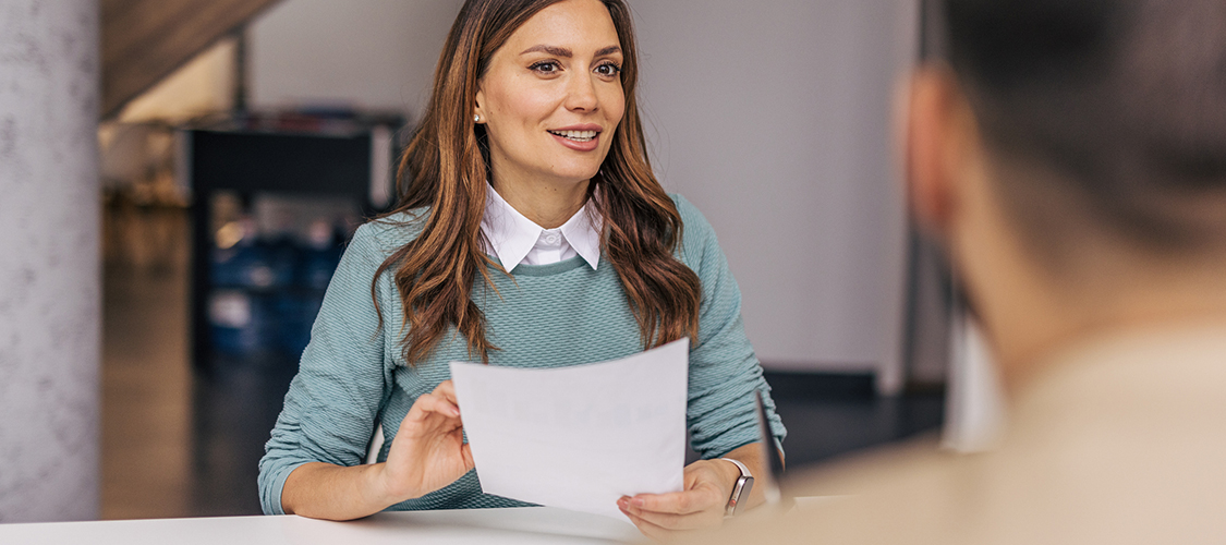 A woman holding up a paper as she sits across from a man.