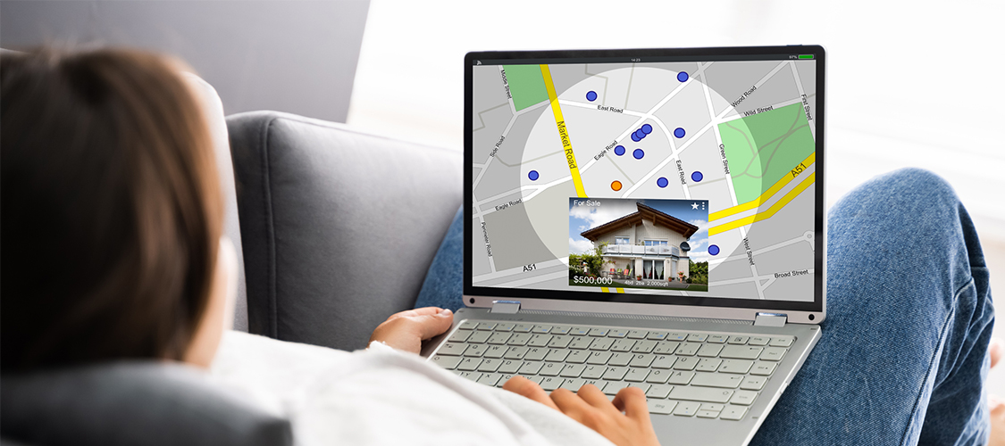 Someone sitting down with a laptop in their lap looking at homes for sale online.