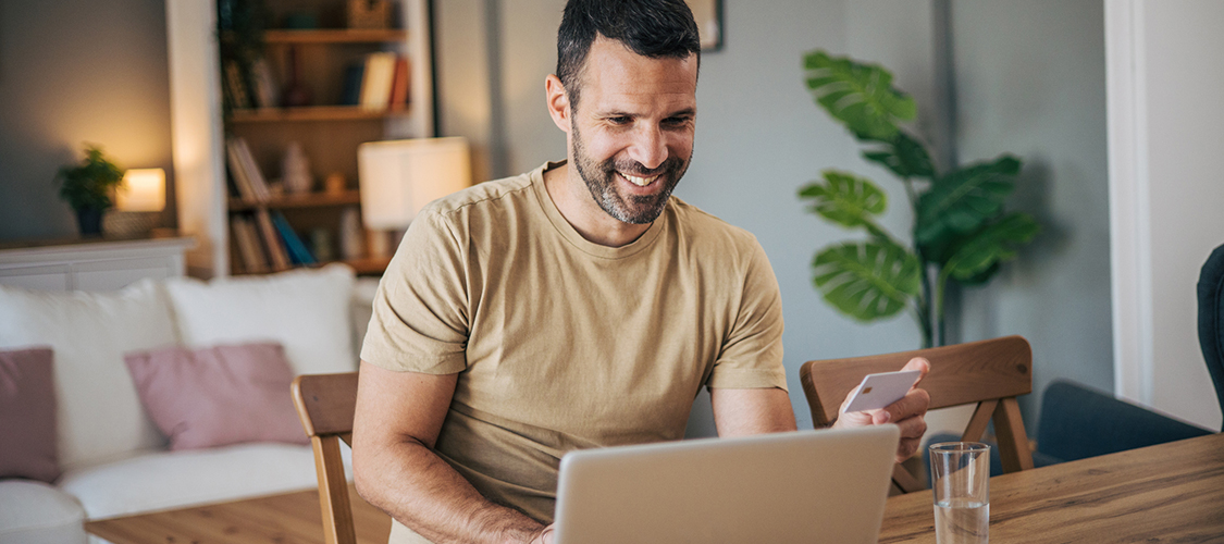 A man smiling as he sits in front of a laptop.