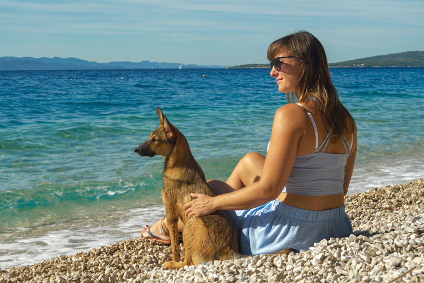 Pes in njegova lastnica sedita na plaži za pse na Hrvaškem.