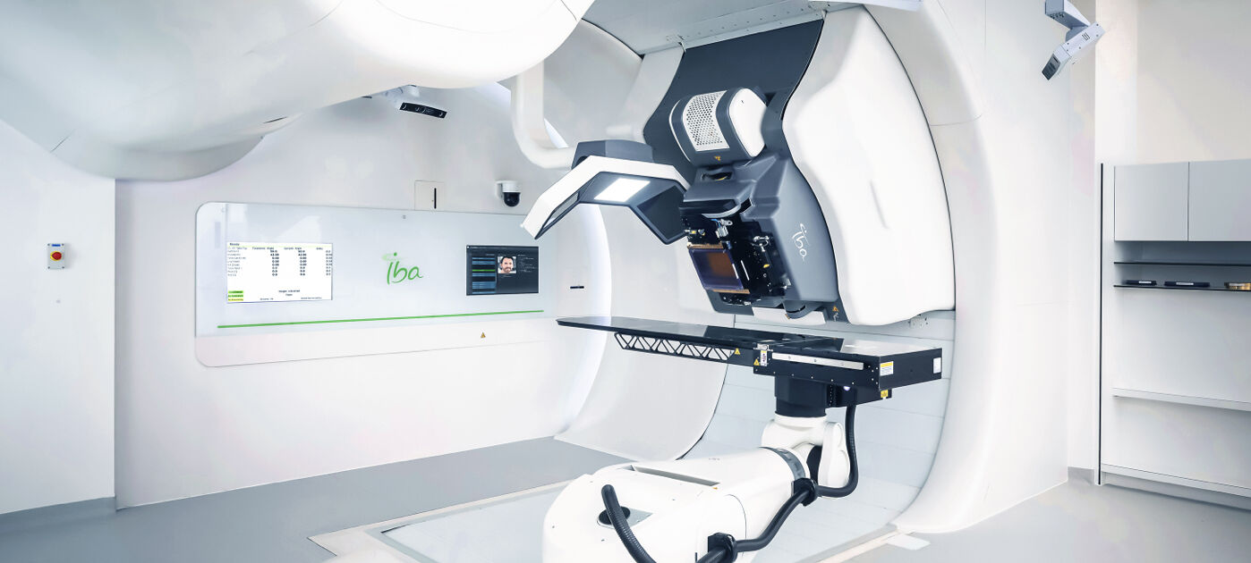 A photo shows a large white machine known as a ProteusONE. The machine features a large gantry, imaging equipment and table for patients to lie upon.