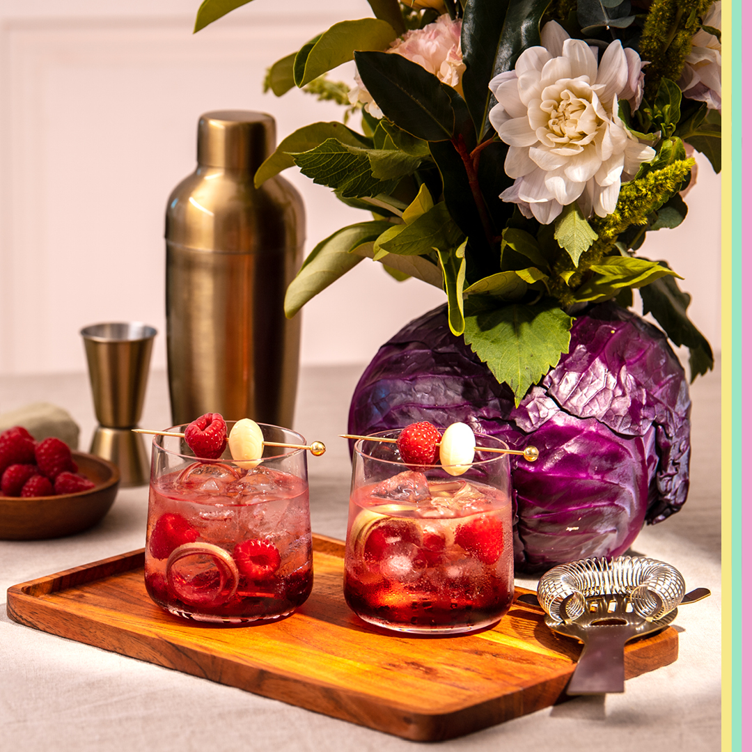 Two cocktail glasses with cocktail shaker raspberries and flowers in cabbage vase