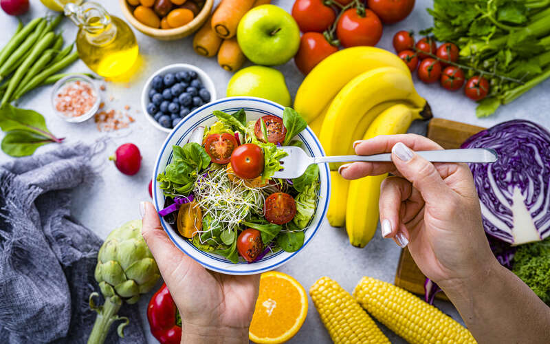 Woman eating fresh rainbow-colored salad. Multicolored fruits and vegetables background. Healthy eating and dieting concept. 