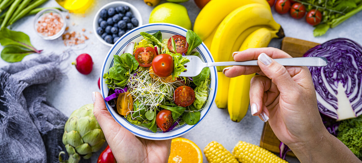 Woman eating fresh rainbow-colored salad. Multicolored fruits and vegetables background. Healthy eating and dieting concept. 