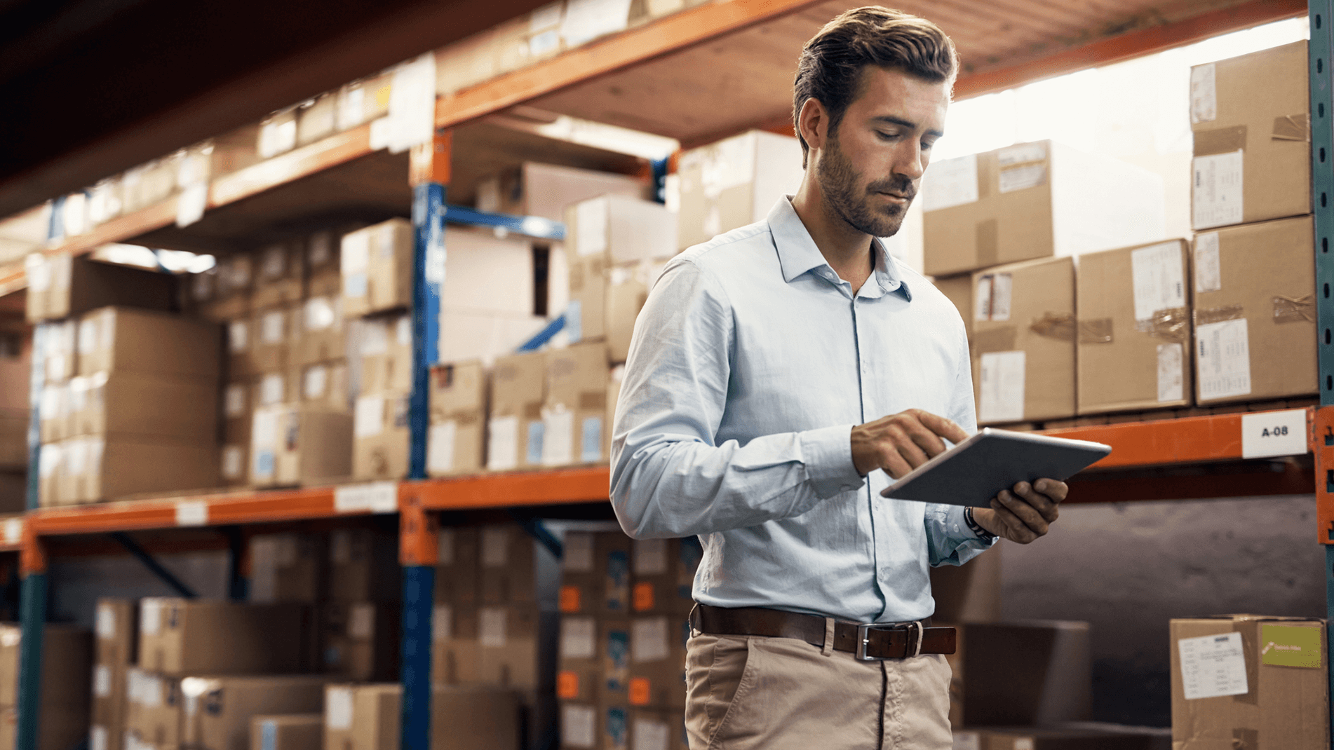 Real-time-Inventory-Promising-In-Page-3.png A man standing in a warehouse looking at a digital tablet.