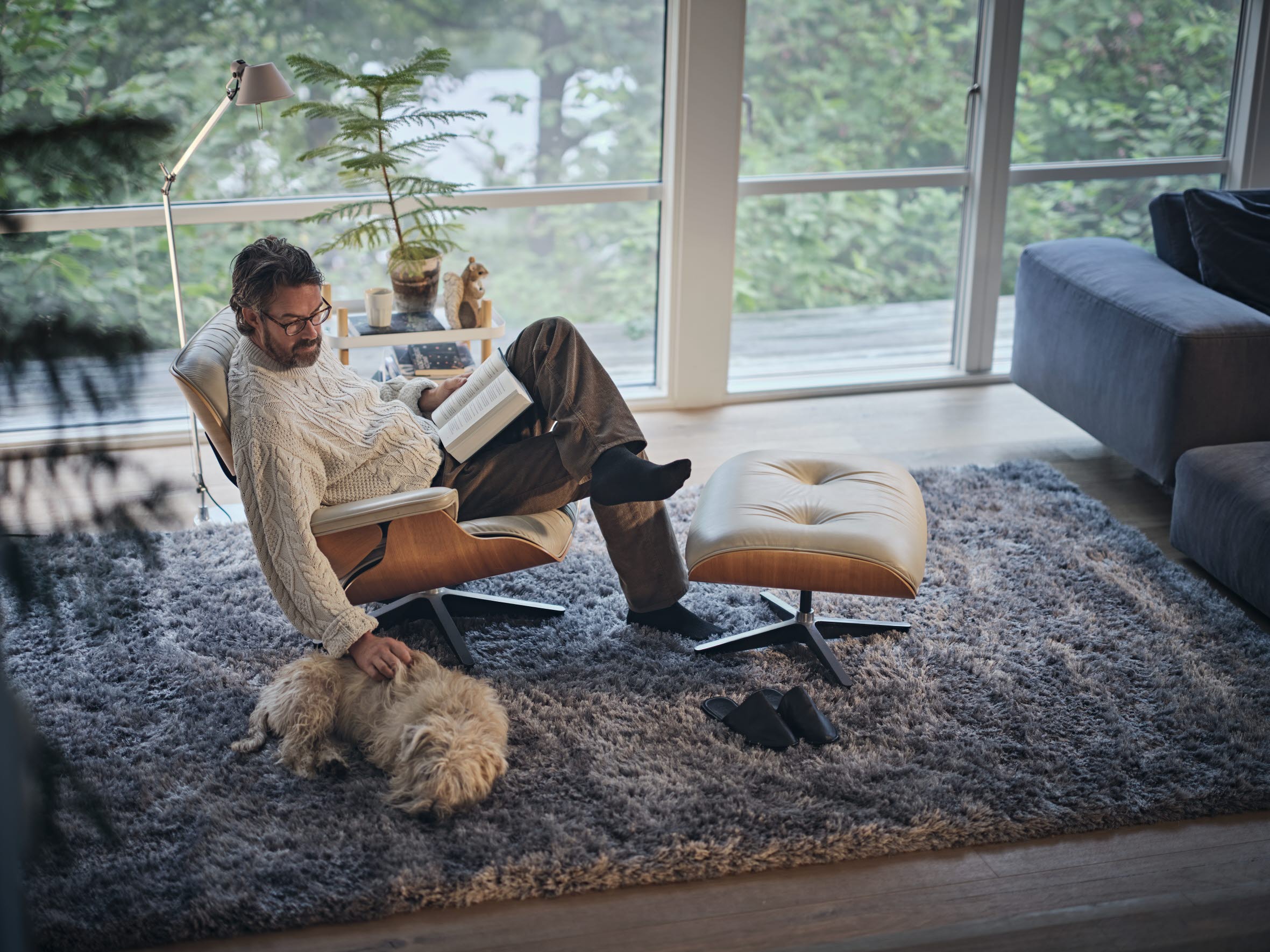 Man sitter i fåtölj och läser en bok och klappar en hund.