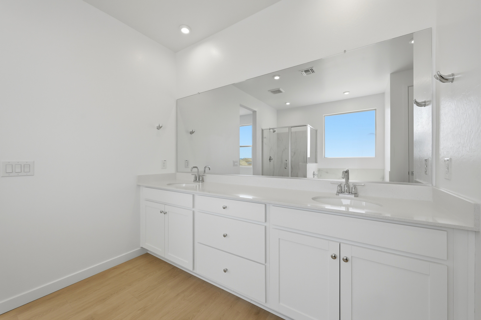 spacious bathroom with wood-like flooring, white cabinets, and chrome faucets