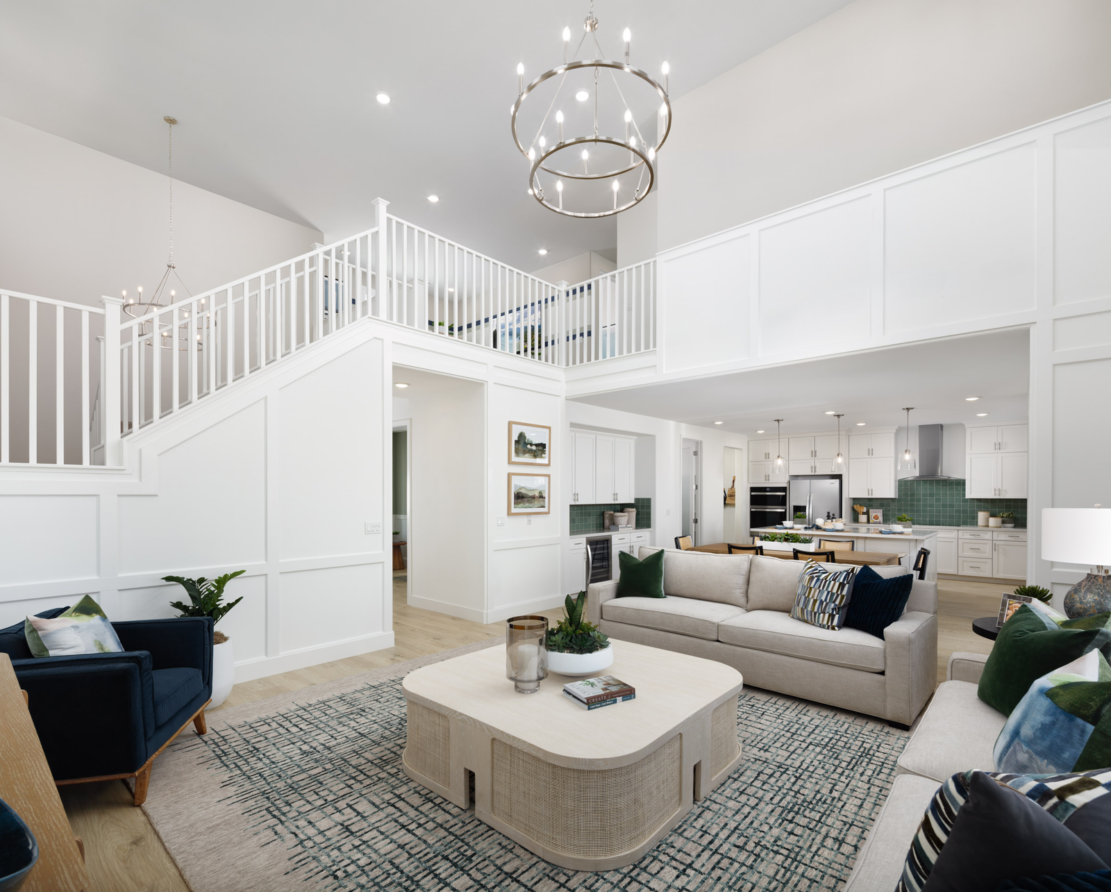 great room with two-story vaulted ceilings, tan sofas, navy blue chair, and view of white staircase