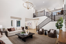 great room with two-story volume ceiling, wood floors, dark wood coffee table, two white sofas, and two brown chairs