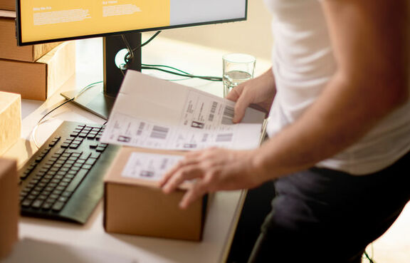 Man attaching a shipping label to a box on a desk in front of a computer