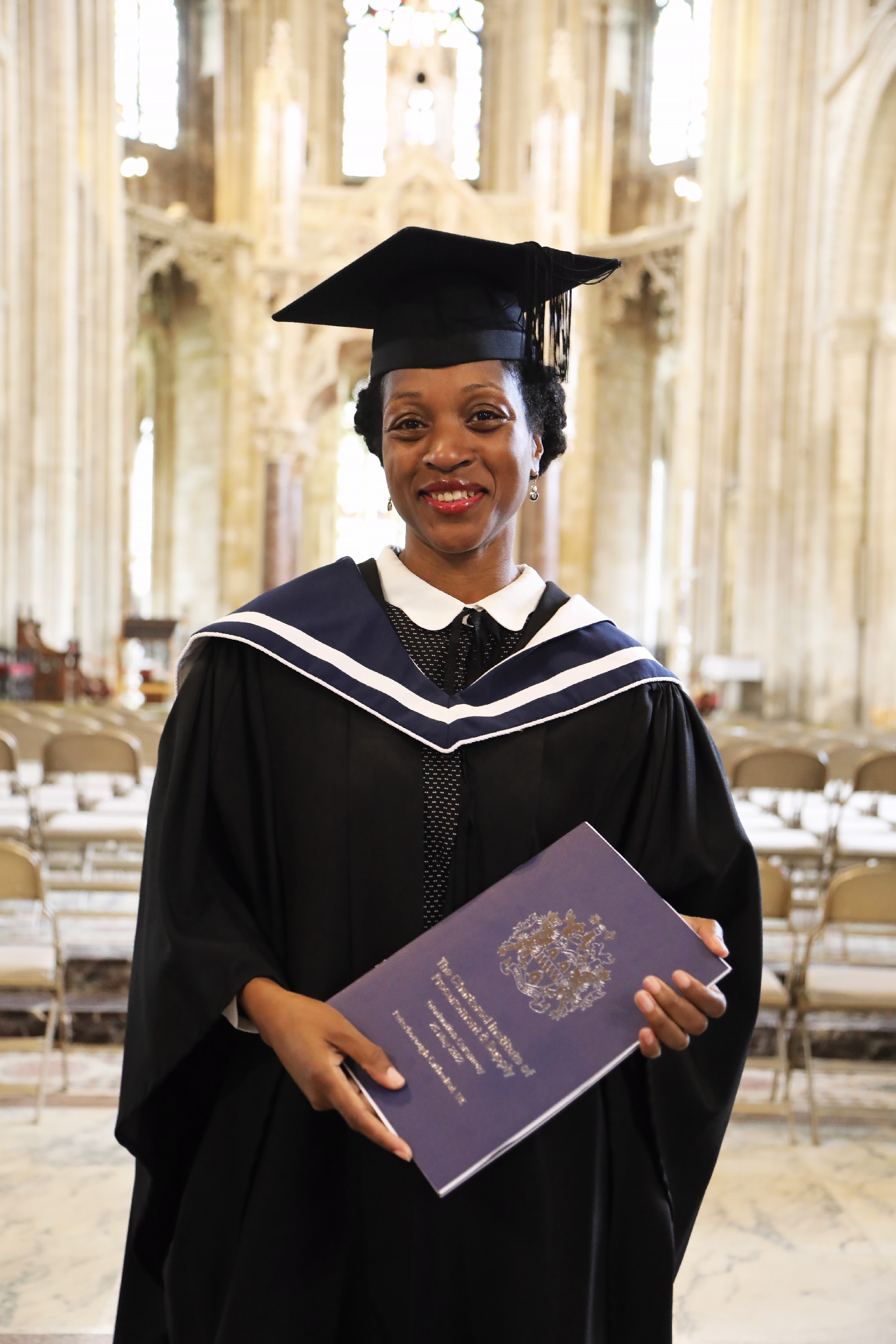 Smiling female graduate holding a diploma folder inside the cathedral