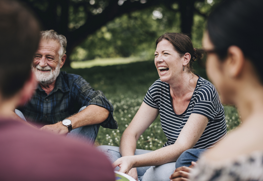 Smiling group of people sitting in a park, talking and laughing together in a relaxed outdoor setting.