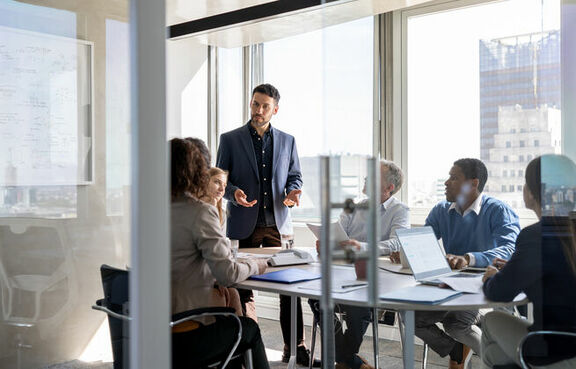 Man talking to a group of professionals gathered around a conference table