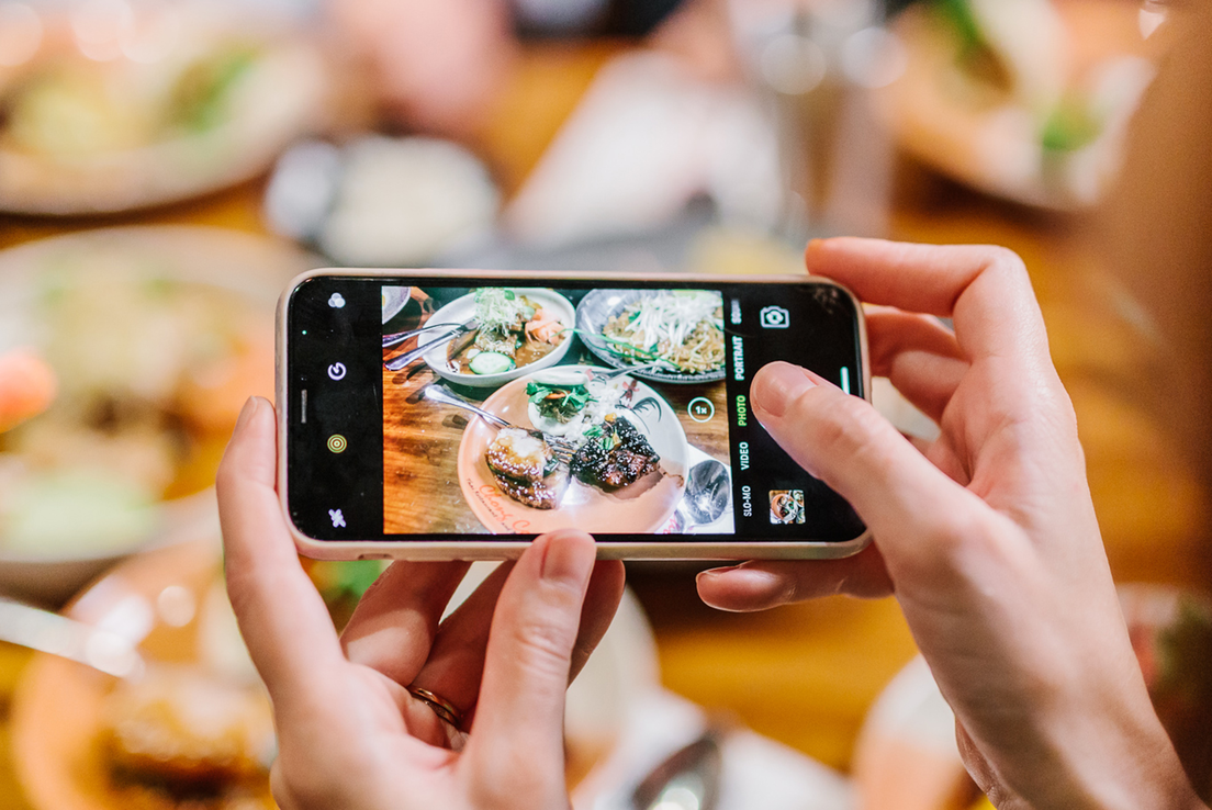 Person holding a phone taking a photo of a table of asian food. 
