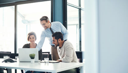 Coworkers sitting at a desk looking at a laptop together