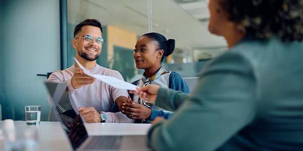 A smiling couple receives paperwork from a loan officer.