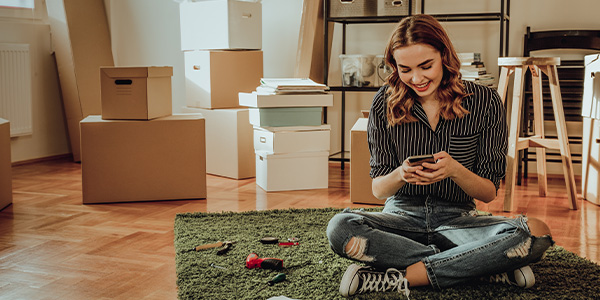 Young woman sitting on the floor of her new home and looking at something on her cell phone