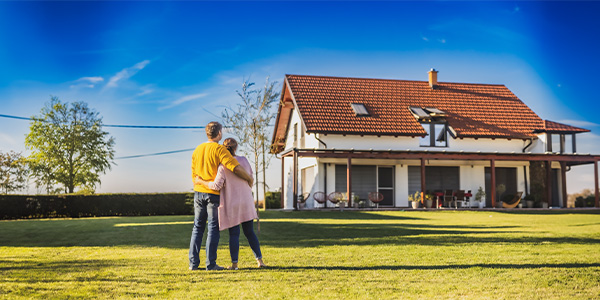 A couple embracing and staring at an older home in the distance.