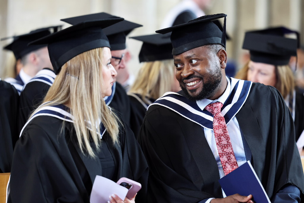 Two happy graduates in gowns and mortarboards talking to each other.