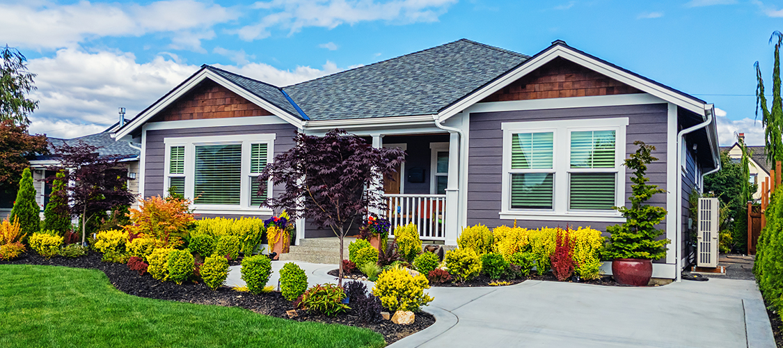 A newly built nice house with grey siding sits on a well-manicured lawn
