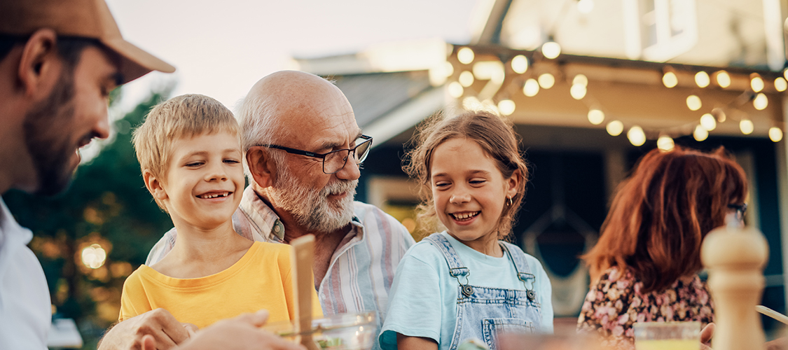 An older man and two young children sit at a table together laughing 
