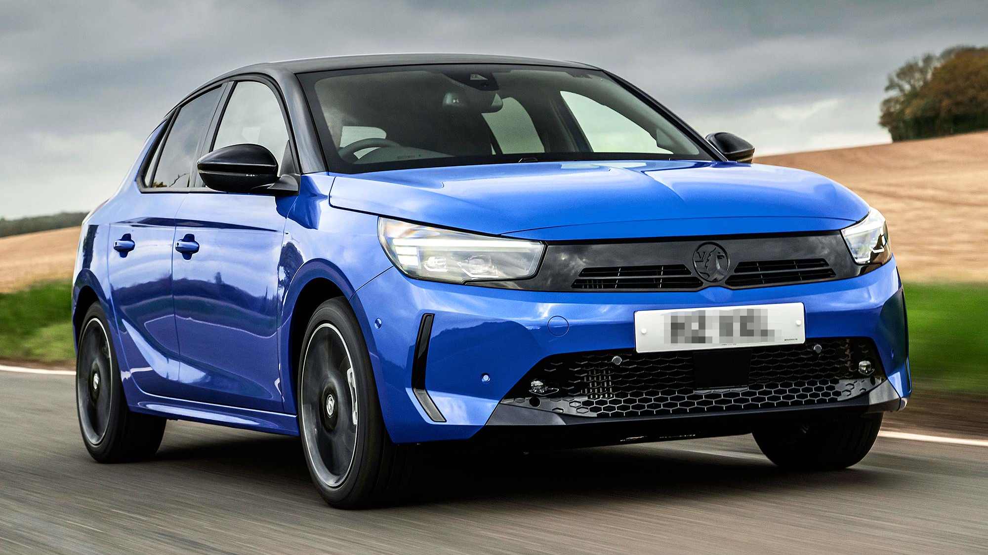 Blue Vauxhall Corsa driving on a country road, front three quarter view, with blurred background showing motion.