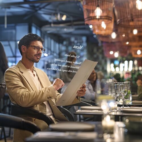 Mann im beigen Anzug trägt HOYA VisuPro-Brille zum Lesen einer Restaurant-Speisekarte