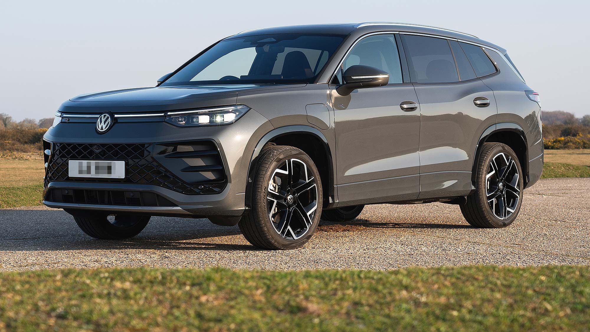 A grey Volkswagen Tayron SUV parked on gravel in an open landscape, front three quarter view, available on the Motability Scheme.