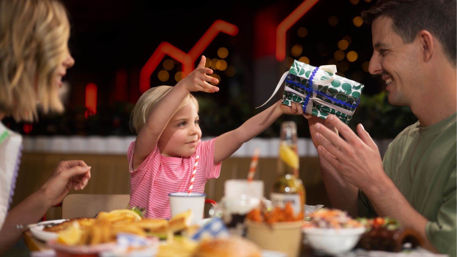 Dad receiving a wrapped Father’s Day gift from a child while sharing a meal together.