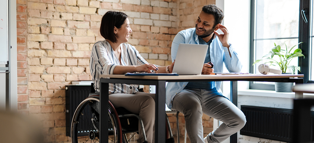 Two colleagues working together at a desk, one using a wheelchair.