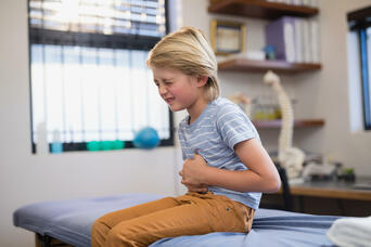 Close-up image of boy clutching his stomach in a doctor's room to illustrate constipation in children.