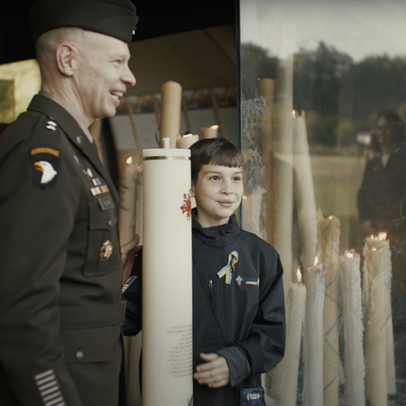 Man in military uniform stands with child at the Lourdes grotto