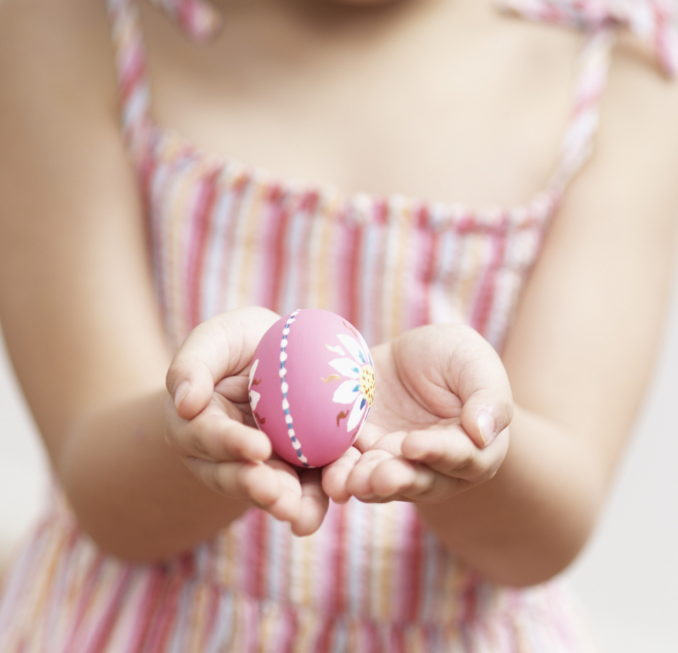 Girl in pink striped dress holds pink decorated easter egg with flower pattern.