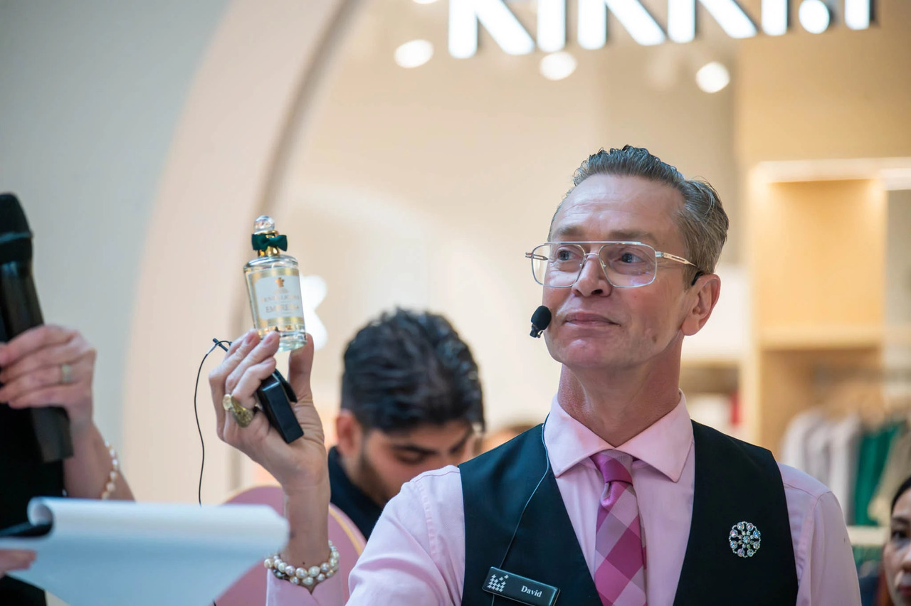 a man with glasses in a pink shirt holding a fancy bottle of fragrance 