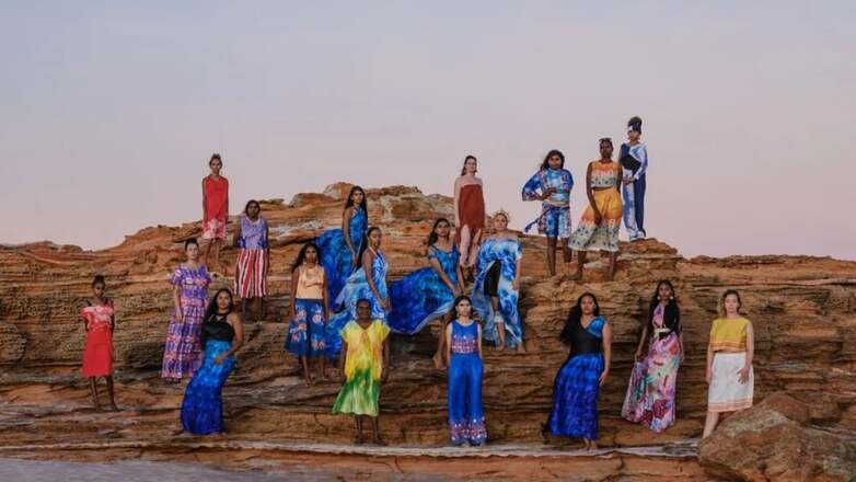 women in colourful first nations designs standing on a rock 