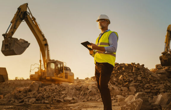 Man in a hard hat and safety vest on a construction site with heavy equipment 