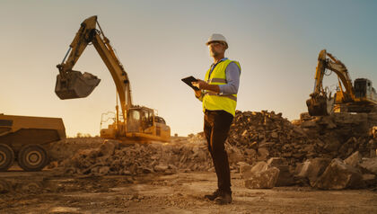 Man in a hard hat and safety vest on a construction site with heavy equipment 