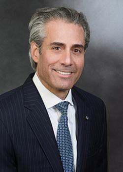 Headshot of David Calzolano, who smiles while wearing a black suit and a blue checkered tie