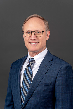 Headshot of David Hanna, who smiles while wearing a dark blue suit and a blue striped tie