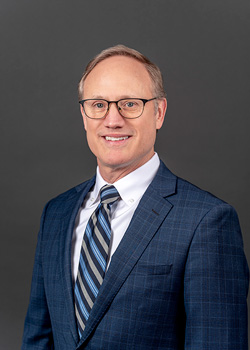 Headshot of David Hanna, who smiles while wearing a dark blue suit and a blue striped tie