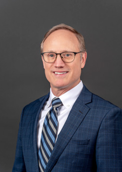 Headshot of David Hanna, who smiles while wearing a dark blue suit and a blue striped tie