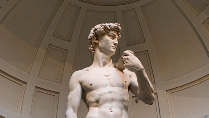 A low-angle view of Michelangelo's marble statue of David, focusing on his torso and head as he looks away under a domed ceiling.