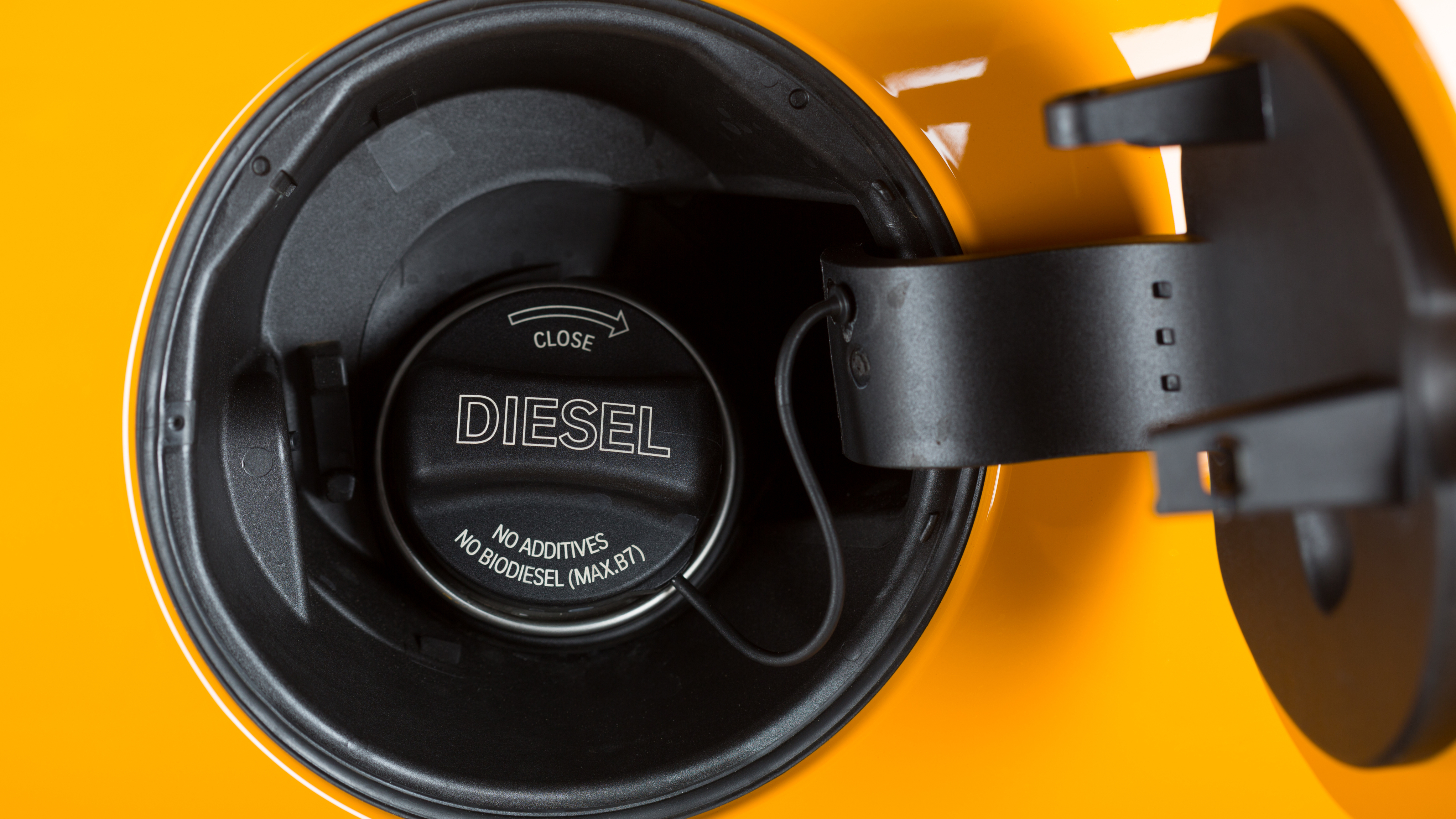 Close-up of a diesel fuel cap on a yellow car, with the fuel filler flap open.