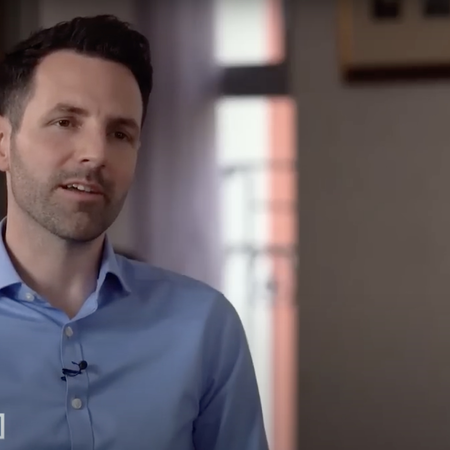 Man in blue button up shirt with a lavalier microphone sits during his interview.