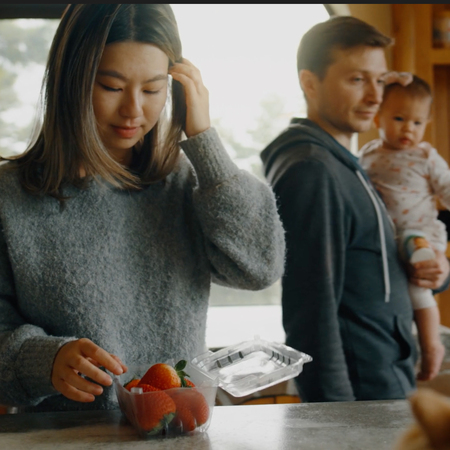 A woman and a man standing at the counter in a kitchen, man holding child.